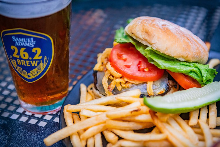 A beer beside a plate of a burger and fries