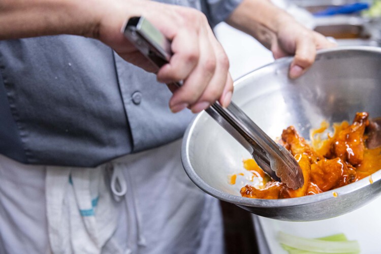 Hands holding tongs marinating chicken