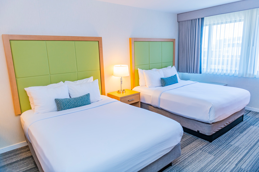 A hotel room with two beds, green headboards, and white bedding.