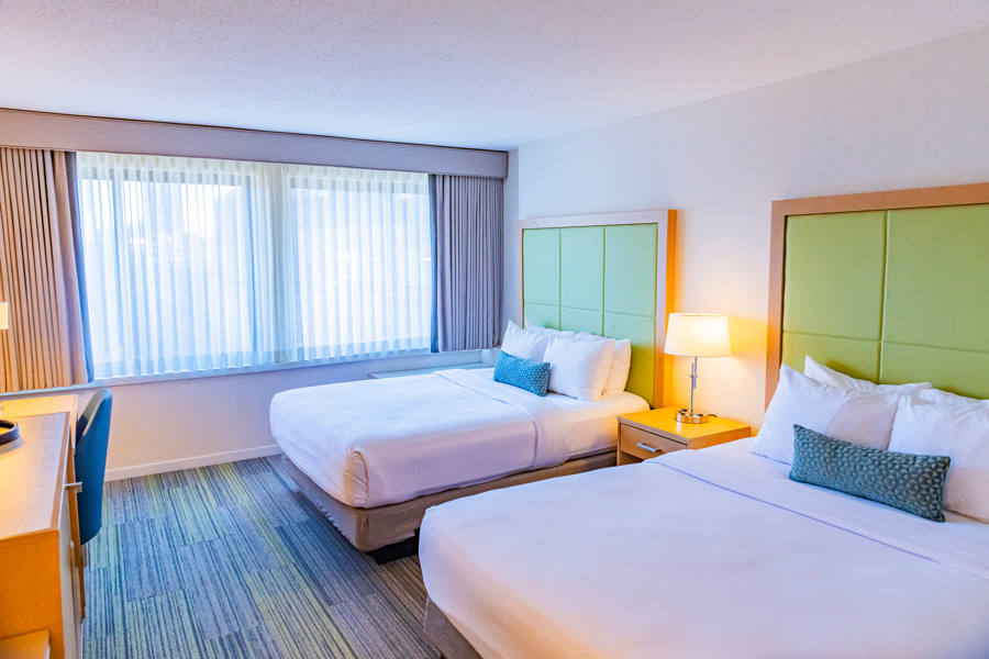 A hotel room with two twin beds, a desk, and a window.