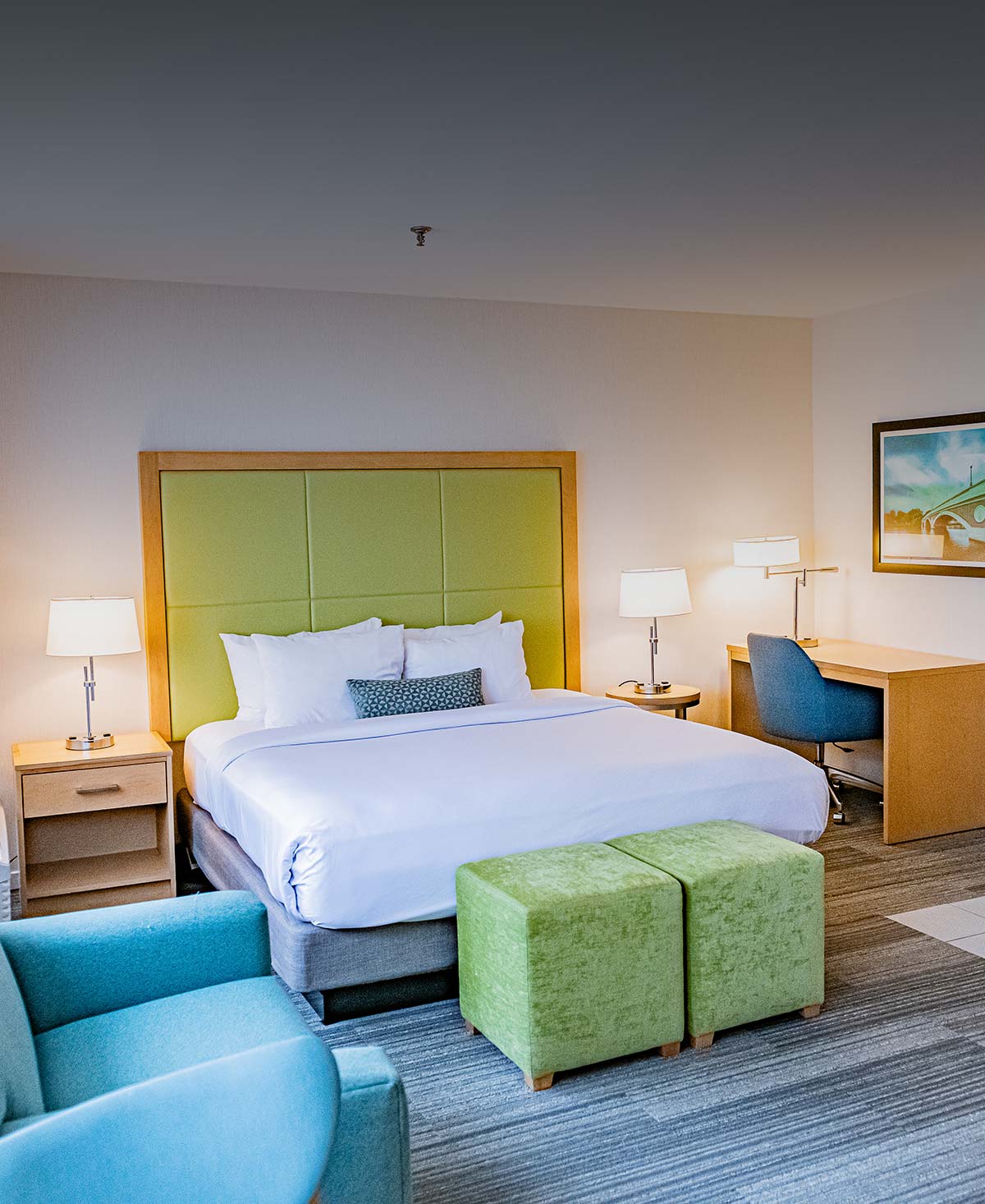 A hotel room with a large bed, desk, chair, and nightstand.