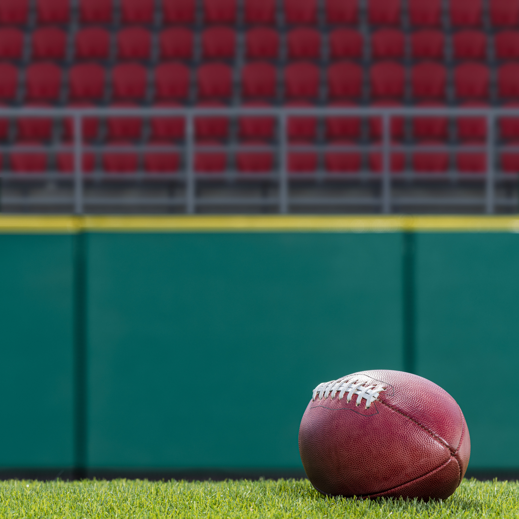 Football on stadium field with red seats in background
